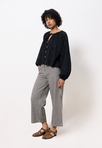 Zwarte, gestructureerde blouse met knoopsluiting, gecombineerd met breedgestreepte zwart-witte broek. Lichtbruine sandalen maken de outfit compleet.