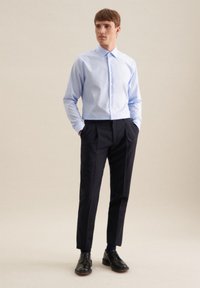 Camicia azzurro chiaro con colletto classico, abbinata a pantaloni eleganti blu navy e scarpe in pelle nere, su uno sfondo neutro.