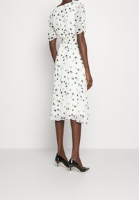 Robe blanche à pois multicolores, avec des manches courtes bouffantes et un ourlet évasé, associée à des escarpins noirs en vernis avec des accents vert fluo.