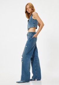 Chaleco de mezclilla recortado con jeans de pierna ancha de talle alto desgastados. Ambas piezas son de un azul claro con bordes deshilachados y detalles de costura visibles.