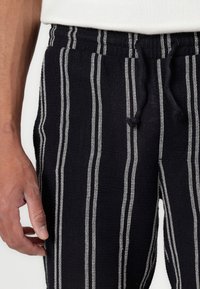 Black and white striped pants made of textured fabric, featuring an elastic waistband with a drawstring for adjustable fit.
