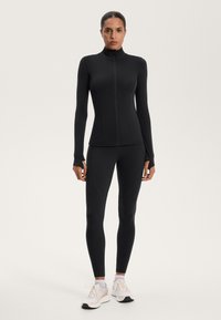 Completo sportivo nero composto da una maglia aderente a maniche lunghe con colletto alto e leggings abbinati, caratterizzati da un tessuto liscio e un design senza cuciture.