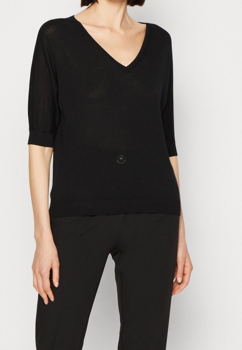 Zwarte gebreide trui met een V-hals, driekwartmouwen en een aangesloten zoom. Heeft een centrale accentknop en een lichte glans in de stof.