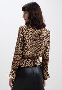 Blusa con stampa leopardata in tessuto simile alla seta, con vita arricciata, maniche lunghe con polsini a campana e una texture liscia e lucida.