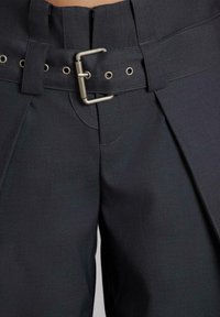 Pantalones gris oscuro con una cinturilla ancha, una hebilla metálica y pliegues visibles. La tela tiene una textura sutil y un diseño estructurado.