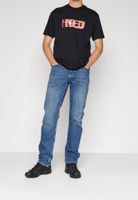 Camiseta negra de manga corta con un estampado gráfico en tonos de rosa, combinada con jeans de mezclilla azul y zapatillas deportivas negras.