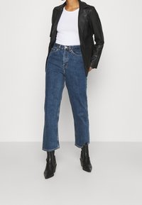 Svart läderblazer över en vit topp, kombinerad med blå raka jeans och svarta stövlar med klack. Texturerade material och figurnära design.