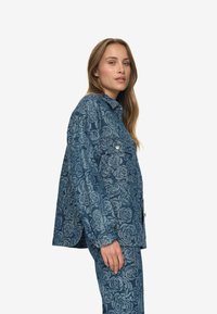 Denim jakna s cvetličnim vzorcem, temno modre barve, sproščenega dizajna, z zapiranjem na gumb in žepi na prsih. Mehka tekstura in rahlo ohlapen kroj.