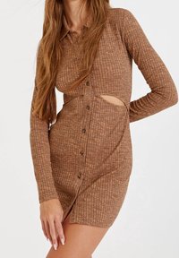 Robe mini marron à côtes, avec manches longues, fermeture boutonnée à l'avant et découpe à la taille. Le tissu texturé ajoute un intérêt visuel.