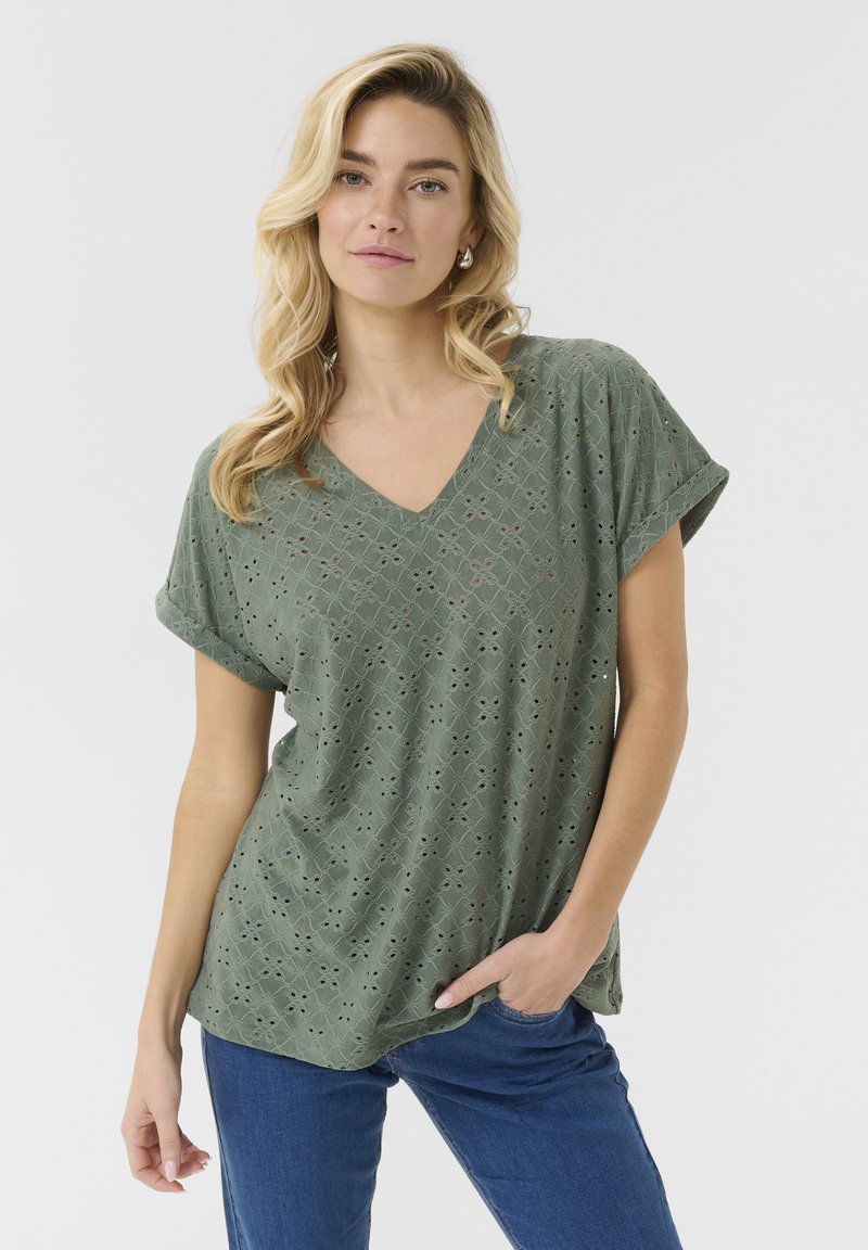 Green v-neck top featuring eyelet embroidery in a geometric pattern, with short rolled sleeves and a relaxed fit. Smooth, lightweight fabric.