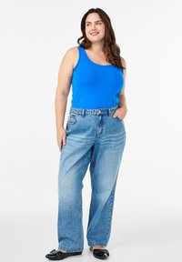 Plavi pamučni top bez rukava u kombinaciji s laganim svijetloplavim trapericama širokog kroja. Model stoji u opuštenom položaju, nosi crne baletanke. Jednostavan stil.