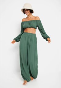 Zeleni kratki off-the-shoulder top z dolgimi rokavi, v kombinaciji s širokimi, flowing zelenimi hlačami. Lahka tkanina in elastičen pas.