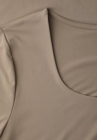 Béžový detail hladké látky oděvu s výstřihem do půlkruhu a prošitým ramenním švem.