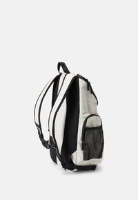 Mochila branca e preta com um bolso lateral em malha, alças ajustáveis e um exterior de tecido suave e durável. Forma curva para um ajuste ergonómico.