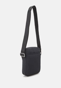 Schwarze Umhängetasche aus strapazierfähigem Stoff, mit einem Reißverschlussverschluss, verstellbarem Tragegurt und einer Vordertasche. Glatte Textur, rechteckige Form.