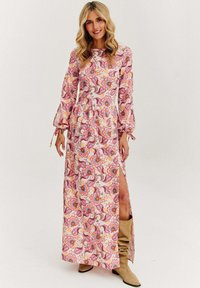 Maxi šaty s květinovým vzorem v růžové a oranžové barvě, dlouhými rukávy s rozšířenými manžetami a s bočním rozparkem. Vyrobené z lehkého materiálu.