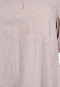 Camicia beige a maniche corte realizzata in tessuto leggero, con taschino sul petto e una vestibilità rilassata con una leggera trama.