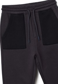 Donkergrijze jogginbroeken met zwarte stoffen zakken, elastische tailleband en trekkoord. Zachte textuur, casual ontwerp geschikt voor comfort.