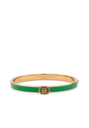Złota bransoletka typu bangle z zielonym emaliowanym paskiem i złotym emblem, ozdobiona małymi kryształkami na środku z przodu.