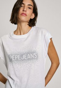 Bílý tričko s krátkým rukávem vyrobené z měkké látky, s nápisem "PEPE JEANS" vytištěným šedým vystouplým písmem na přední straně.