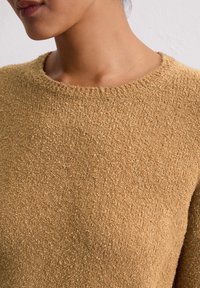Textured, mustard-colored sweater with a round neckline and visible stitching detail. Soft fabric appears warm and cozy, with a simple design.