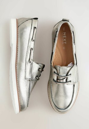 Scarpe argento metallizzato con tomaia sintetica, lacci frontali e suola bianca. Presentano cuciture a contrasto e una punta arrotondata.