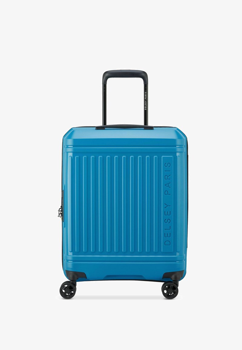 Valigia rigida blu con scanalature verticali, manico superiore, quattro ruote e una cerniera laterale. Nome del marchio "Delsey Paris" impresso sul davanti.
