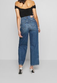 Korkeavyötäröiset siniset farkut, joissa on leveät lahkeet, yhdistettynä mustaan hartiat paljastavaan paitaan. Huomionarvoinen merkki takana ja hopeiset korkeat sandaalit.