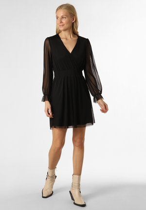 Schwarzes Kleid mit Wickeldesign, durchsichtigen langen Ärmeln und tailliertem Schnitt. Getragen mit beigen Knöchelstiefeln mit einem einzigartigen Riemendetail.