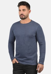 Marineblauw langsloven shirt in een gestructureerde stof met een gesprenkeld patroon. Ronde halslijn, slim fit ontwerp en ribgebreide manchetten. Gecombineerd met donkere spijkerbroek.