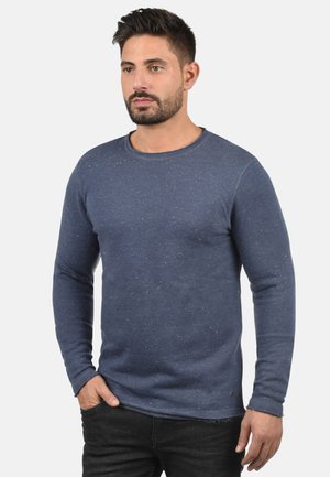 Marineblauw langsloven shirt in een gestructureerde stof met een gesprenkeld patroon. Ronde halslijn, slim fit ontwerp en ribgebreide manchetten. Gecombineerd met donkere spijkerbroek.