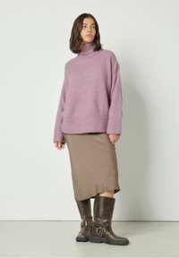 Šviesiai violetinė per didelė megztinė su aukštu kaklu, tekstūruota, dėvima ant prigludusios rudos sijono. Rudos odinės iki kelių botas su sagties akcentais.