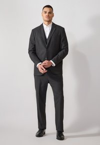 Dunkelgrauer Anzug mit taillierter Blazerjacke und geraden Hosen. Strukturierter Stoff, einreißiges Design und weißes Hemd unter der Jacke.