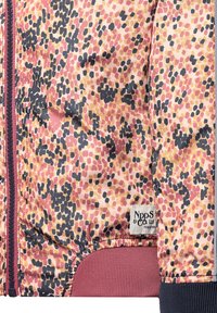 Primo piano di un giubbotto maculato rosa, beige e nero con zip bordeaux, orlo a coste, polsini e un'etichetta del marchio cucita di lato.