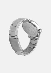 Montre en acier inoxydable avec un bracelet en maillons métalliques, un cadran rond et un logo gravé au dos. Présente une finition polie et un fermoir sécurisé.