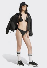 Juodo bikinio viršus ir apačia, derinami su juoda bombere striuke. Juoda kepurė, dryžuotos aukštos per kelius kojinės ir juodi sportbačiai.