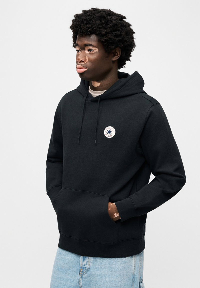 Sort hættetrøje lavet af bomuldsblanding. Har en kængurulomme, hætte med snøre og et rundt logopatch på brystet.