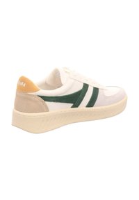 Vit sneakers med gröna mocka detaljer, beige häl och texturerad gummisula. Har en framträdande logotyp på hälen.