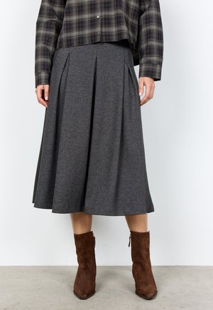 Woman wearing a gray pleated midi skirt, brown suede ankle boots, and a dark plaid button-up shirt.