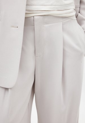 Chaqueta y pantalones de traje de color gris claro, con una textura suave, pantalones de frente plano y un discreto detalle en los bolsillos.