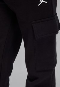 Pantaloni negri cargo din material moale, cu un buzunar lateral și un logo alb Jumpman pe coapsă. Cusături plate și croială ajustată.