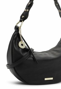 Borsa a mano in pelle nera a forma di mezza luna con cerniera dorata, borchie dorate sulla tracolla e un'etichetta rotonda dorata del marchio appesa a una catena.