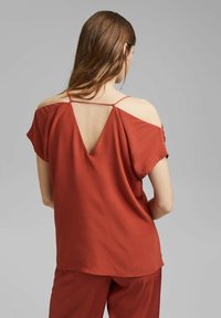 Blusa de color óxido con mangas cortas, hombros al aire y espalda en forma de V. Confeccionada en un tejido ligero de textura suave y corte casual.