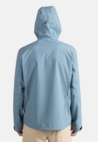 Ljusblå vattentät jacka med huva, med en slät yta och minimalistisk design. Inkluderar justerbara ärmslut och logotypdetalj.
