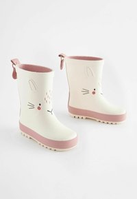 Bottes de pluie en caoutchouc blanc avec semelle rose, présentant un design de tête de lapin, une forme arrondie, des accents texturés et des languettes pour un enfilage facile.
