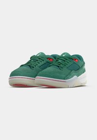 Zelené semišové tenisky s detailmi z priedušnej sieťoviny, bielou medzipodrážkou, červenými očkami na šnúrky a textúrovanou podrážkou. Vyznačujú sa minimalistickým dizajnom a detailom loga.