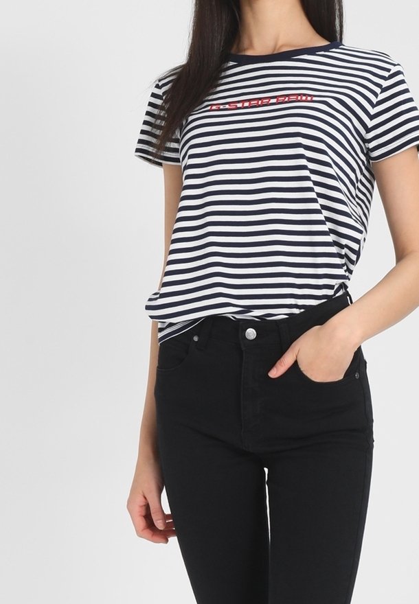Camiseta de algodón con rayas verticales en navy y blanco, escote redondo y detalle en texto rojo en el pecho. Combinada con jeans negros.
