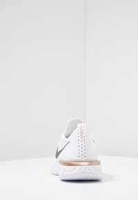 White athletic shoe with a textured knitted upper, black Swoosh logo, and a metallic copper accent on the heel, featuring a patterned sole.