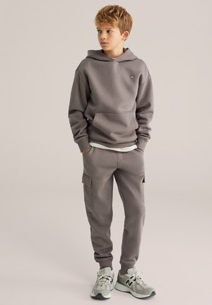 Un sweat à capuche gris avec une poche kangourou et un logo, associé à un pantalon cargo assorti avec des poches latérales, complété par des baskets grises.