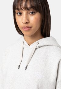 Light grey hooded sweatshirt with a textured finish, featuring a small white logo on the chest, and contrasting drawstring accents.